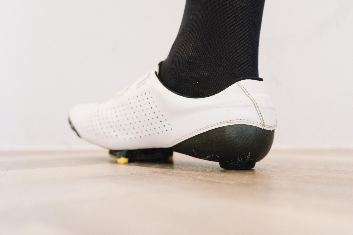 A close up of a white cycling shoe with a black socked foot in it