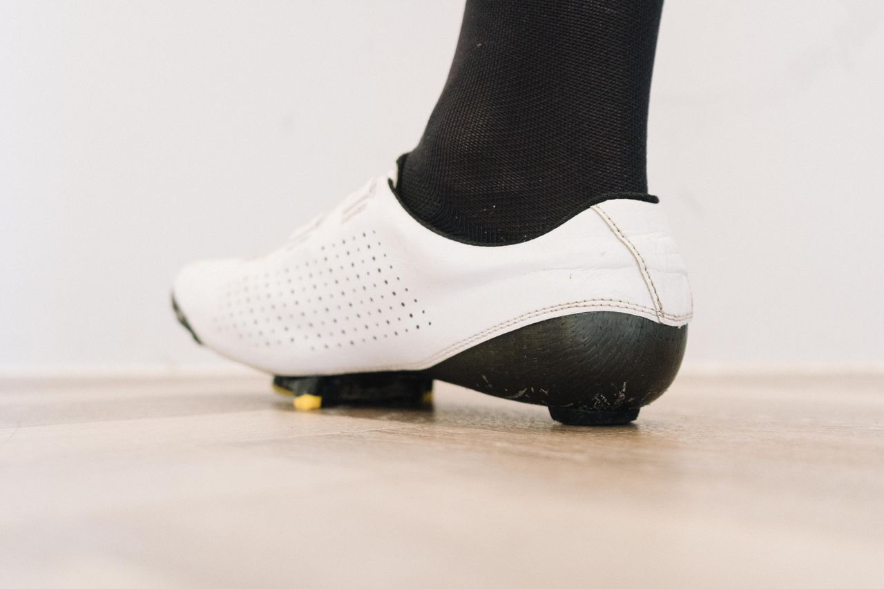 A close up of a white cycling shoe with a black socked foot in it
