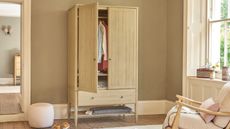 Free standing oak wardrobe in a beige room with an arm chair beside it 