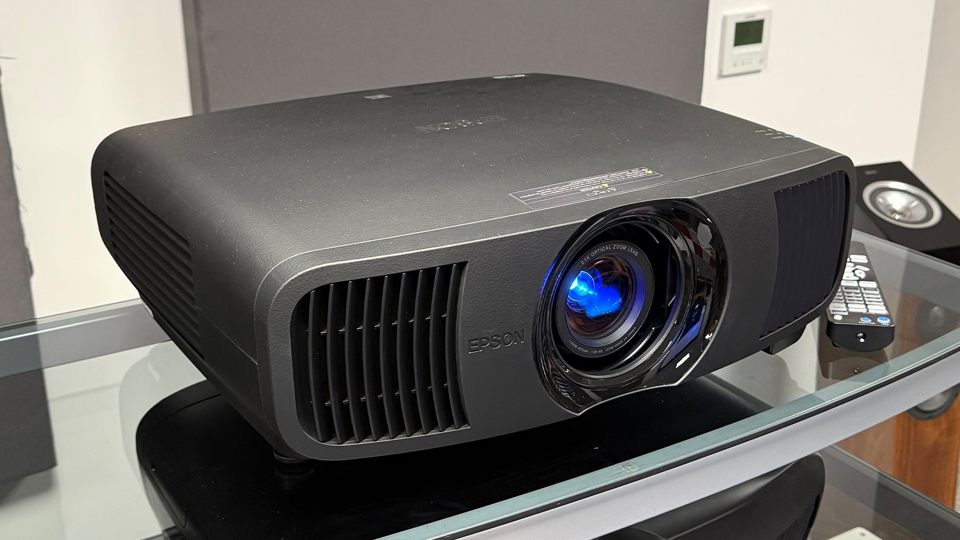 Epson EH-LS9000 home cinema projector on glass AV rack with remote control next to it
