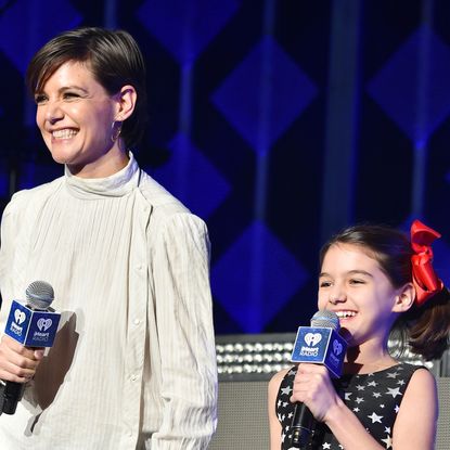 Katie Holmes smiles while wearing a floaty white shirt and holding hands with daughter Suri Holmes, who is wearing a navy dress covered in white stars