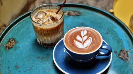 A latte on a table next to an iced coffee