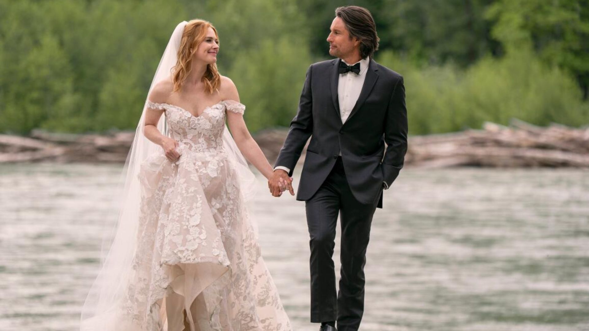 Mel and Jack hold hands walking by the river