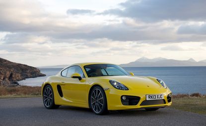 A yellow Cayman S with water and mountains in the background