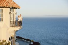 A retired couple stands on the balcony of their vacation home.