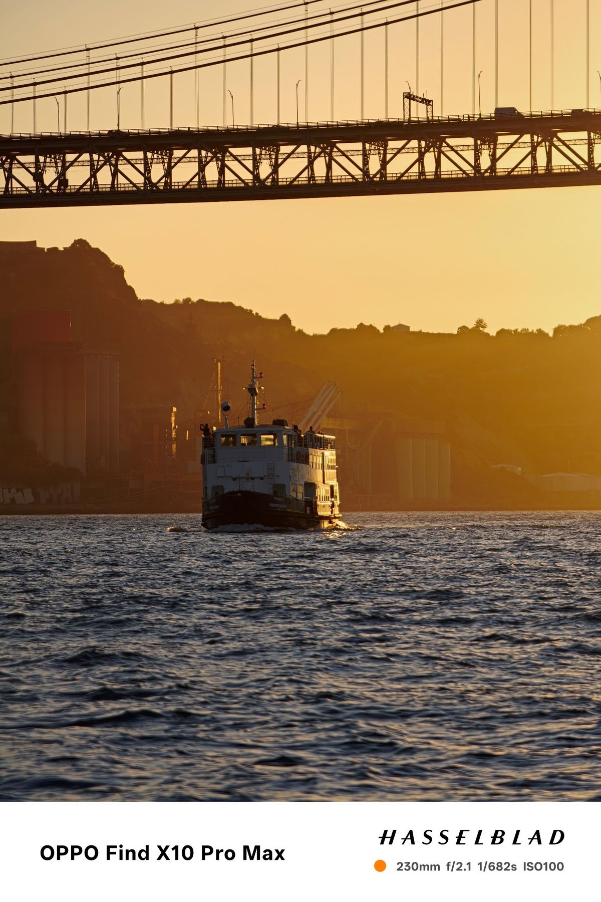 Ferry traveling beneath the 25 de Abril Bridge in warm golden-hour light.