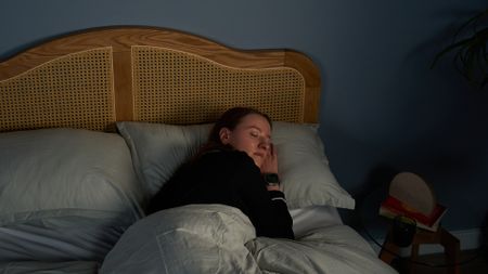 A woman with long brown hair sleeps on her side on a comfortable pillow in a blue bedroom at night
