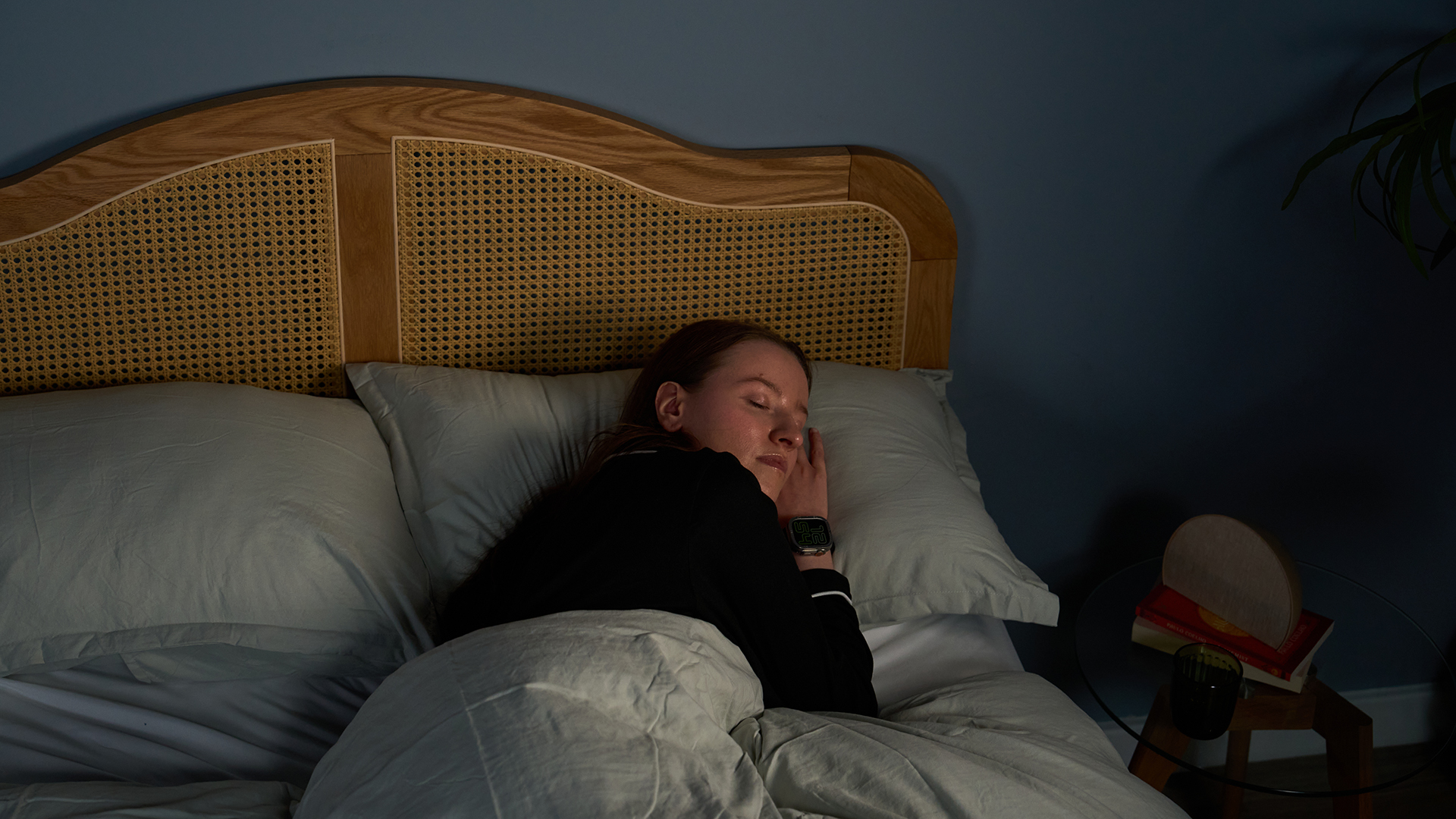 A woman with long brown hair sleeps on her side on a comfortable pillow in a blue bedroom at night