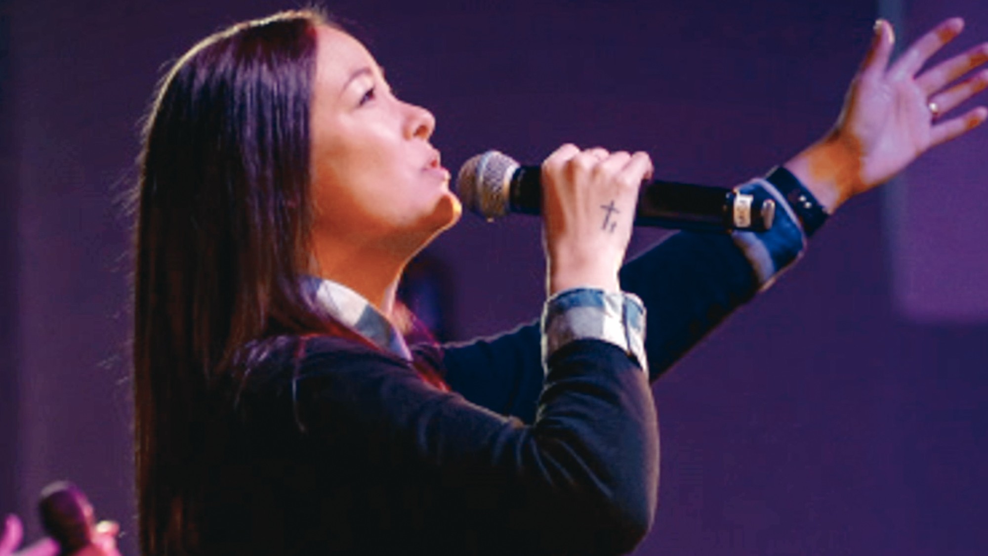 Mica Miller singing into a microphone and holding her arm up