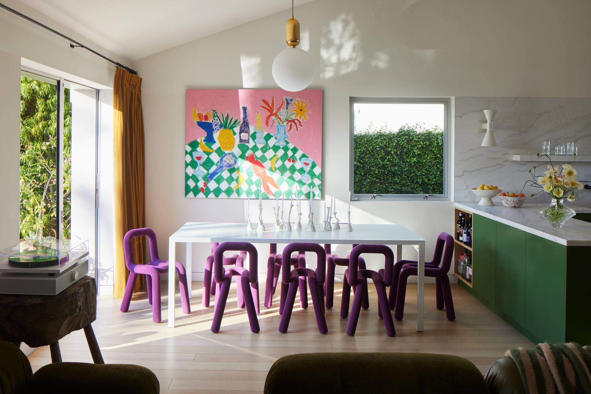 A white, open living, dining, kitchen space with a bright artwork on the wall and bright purple chairs.