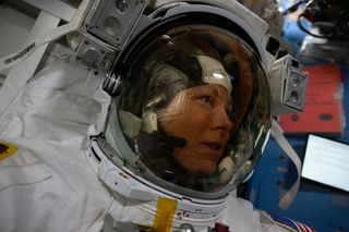 closeup of a female astronaut wearing a spacesuit, focusing on her face through the dark but transparent faceplate