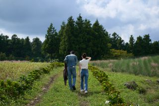 A man and a woman wearing denim outfits walk with their backs to the camera, through a grassy field.