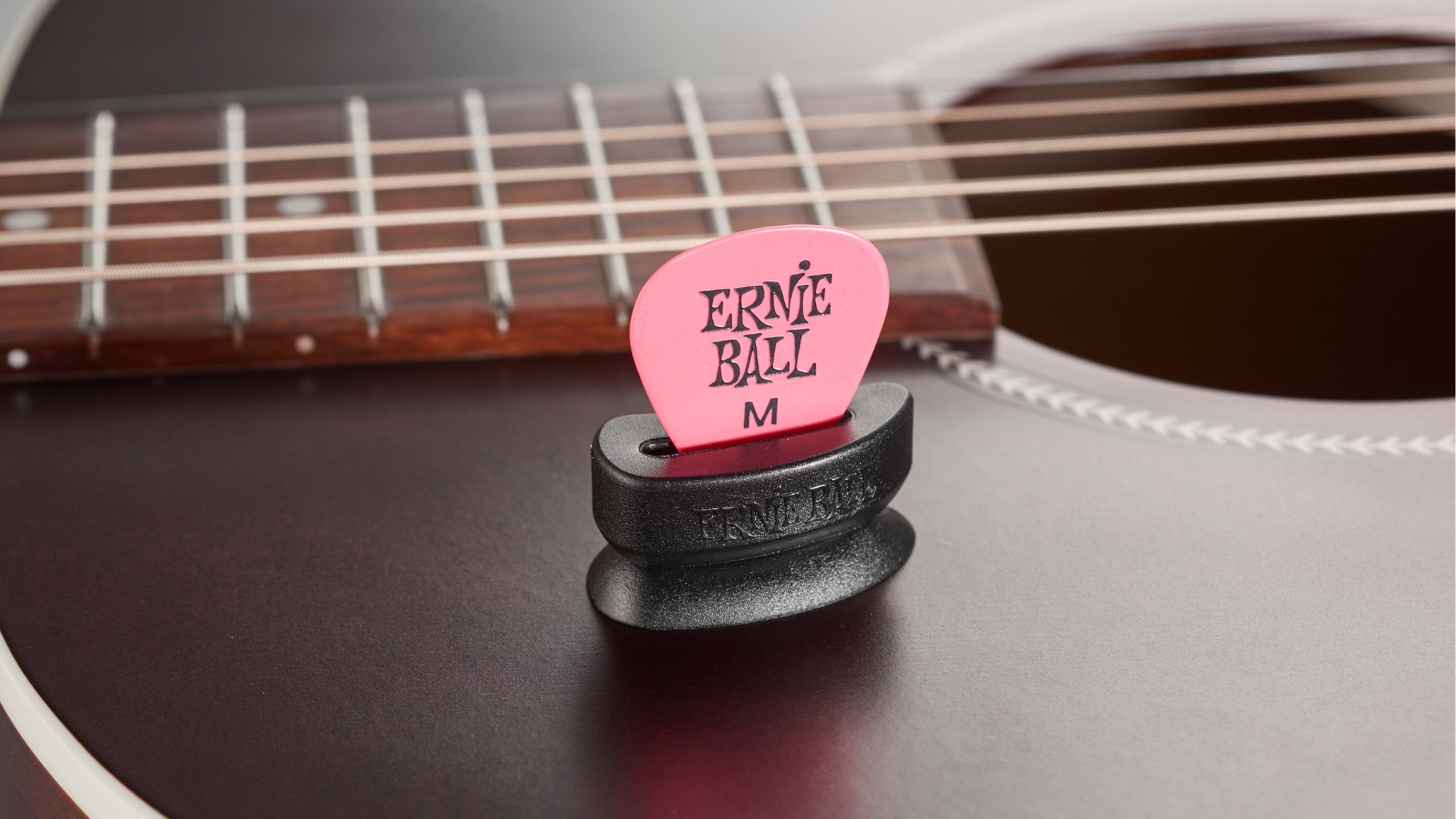An Ernie Ball guitar pick in a holder attached to an acoustic guitar