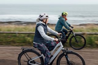 A side view of a group of women who are enjoying a staycation to Bamburgh and Ambleside in the North East of England. They are riding electric bikes and taking in the scenery along the quiet coastal route