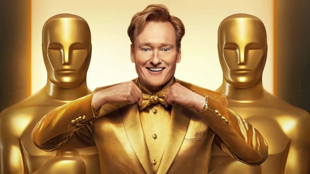 98th Academy Awards host Conan O'Brien wearing a gold tuxedo standing alongside two human-sized Oscar statuettes in a promotional image for the 2026 Oscars.