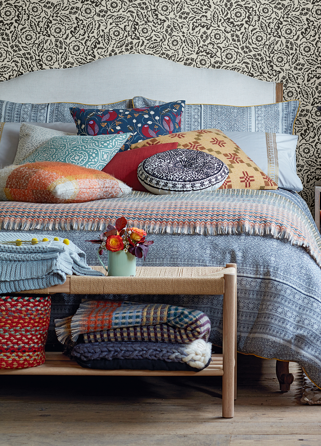 bedroom with patterned wallpaper with blue patterned bedding with folk-style embroidered cushions and knitted blankets