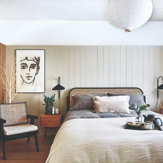 A neutral betroom with a white ceiling and a beige-painted panelled wall behind a rattan bed