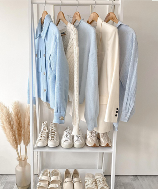 A white clothing rack with light neutral and white clothes styled next to pammpas grass