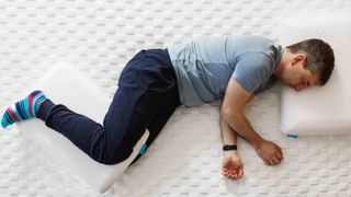 A man lies on his side in 'Dreamer' position with a pillow between his knees