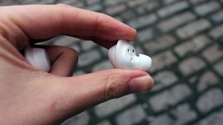 A close up of a single one of the Samsung Galaxy Buds that someone is holding between their thumb and forefinger