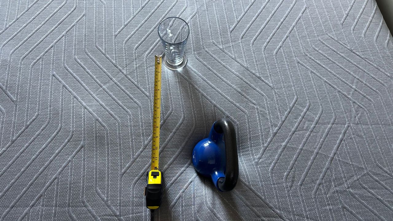 A blue weight, yellow measuring tape, and a glass sit on the EGOHOME Black 12" Mattress ready for a motion isolation test to begin.