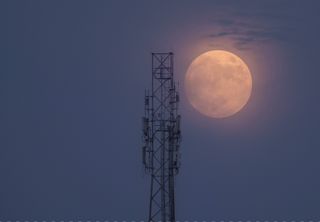 Super Blue Moon shines a hazy orange next to a tower.