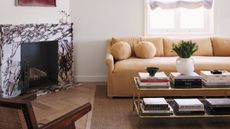 smaller living room with fireplace on diagonal wall, sofa, coffee table stacked with books, and timber accent chair 