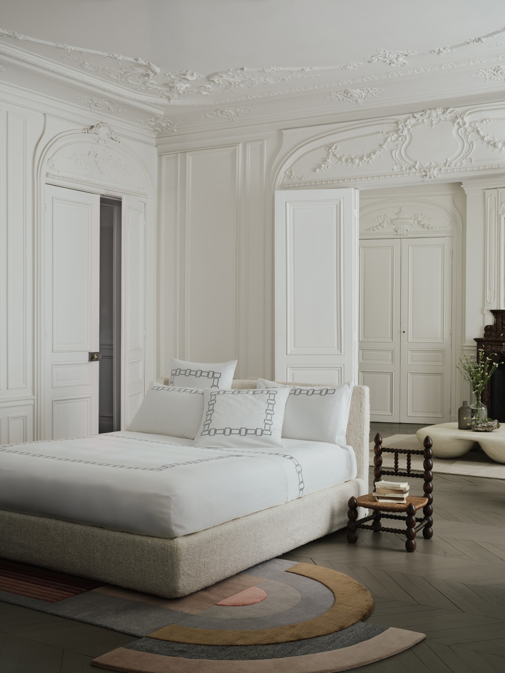 Image of a white bed with white bedding in a large, luxurious-looking room. The walls of the room are white with intricate molding.