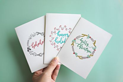 Cropped Hand Holding Christmas Cards With Text Over Turquoise Background