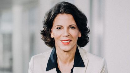 Alexandra Palt in a white suit, looking at the camera, smiling 