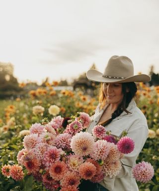 Kelsey Hall in a cowboy hat holding a large bunch of pink, blush and salmon dahlias