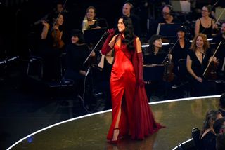 Dua Lipa onstage in London with black hair while wearing a red dress