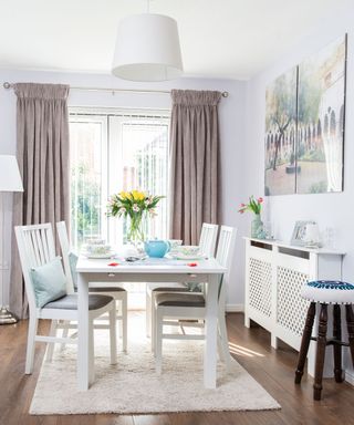 Dining room with white walls, wooden floor, white table and chairs and taupe curtains