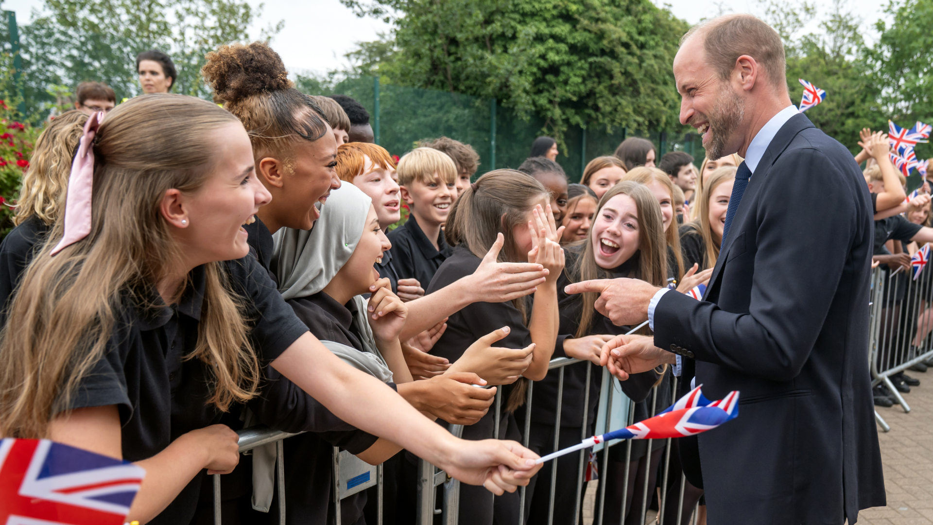 Prince William talking to a crowd of kids screaming and waving flags