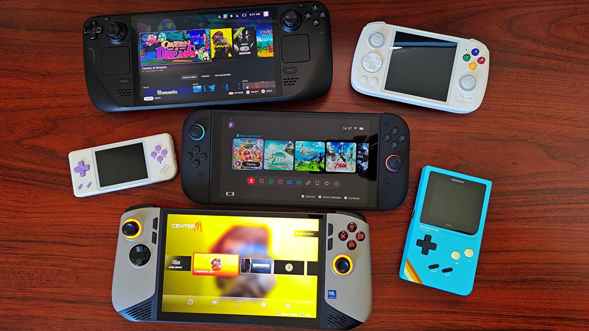 Nintendo Switch 2 sitting in centre with Steam Deck OLED above on left, Anbernic RG Cube aboveon right, Anbernic RG28XX directly left, Modretro Chromatic on right, and MSI Claw 8 AI+ below on woodgrain desk.