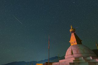 perseid meteor shooting across the sky above a large domed building.