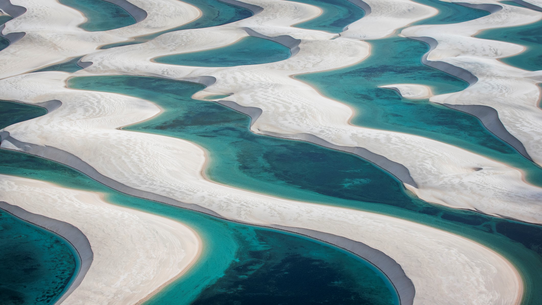 Aerial view of white sand dunes separated by blue pools of water.