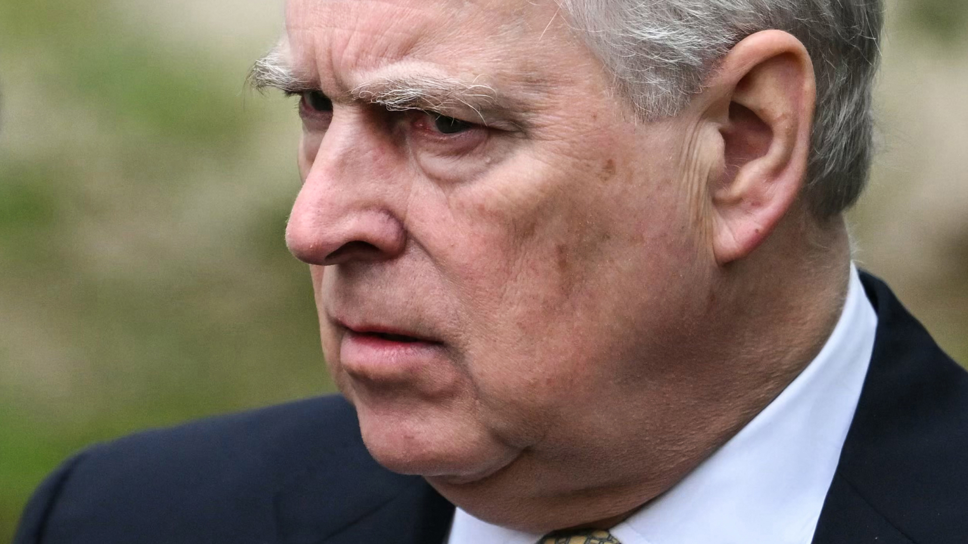 Prince Andrew wears a navy suit with a white shirt and looks pensive or annoyed