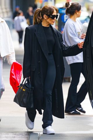 Jennifer Lopez mengenakan sepatu platform sneakers berwarna putih dengan legging dan outfit serba hitam