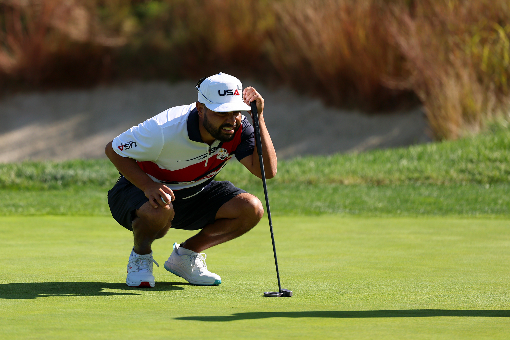 JJ Spaun reading a putt in a practice round for the 2025 Ryder Cup, wearing his red, white and blue Team USA apparel