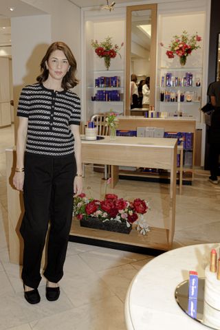 Sofia Coppola standing in front of a display of Sofia Coppola x Augustinus Bader products.