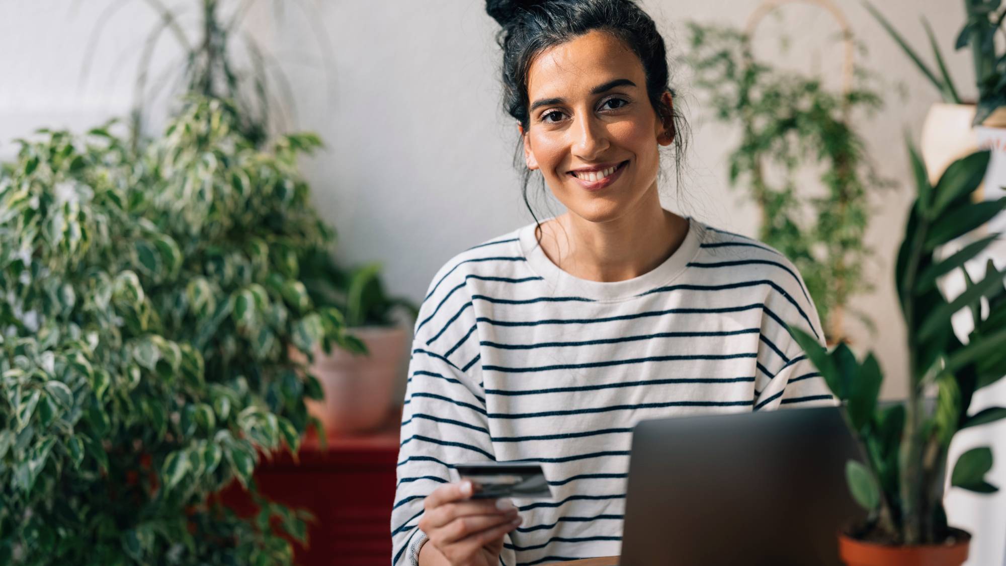 A woman at a laptop smiles holding a credit card