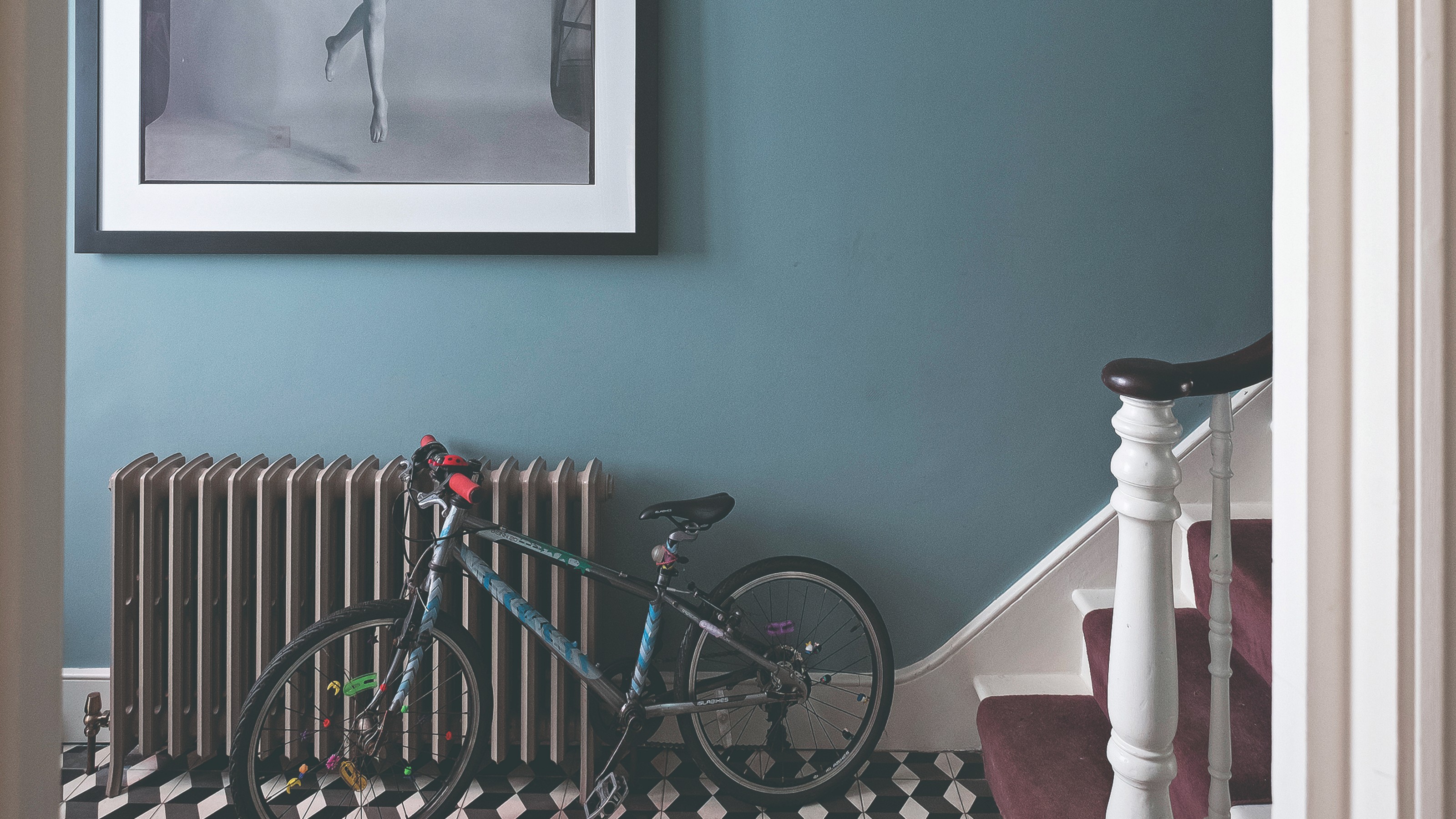 A blue hallway painted in Farrow & Ball's Inchura Blue with a black radiator and graphic tiled floor