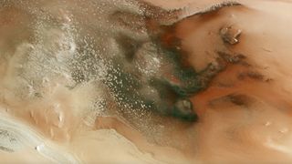 photo of mars from orbit, showing a landscape of red dirt, flecks of white icy and dark deposits