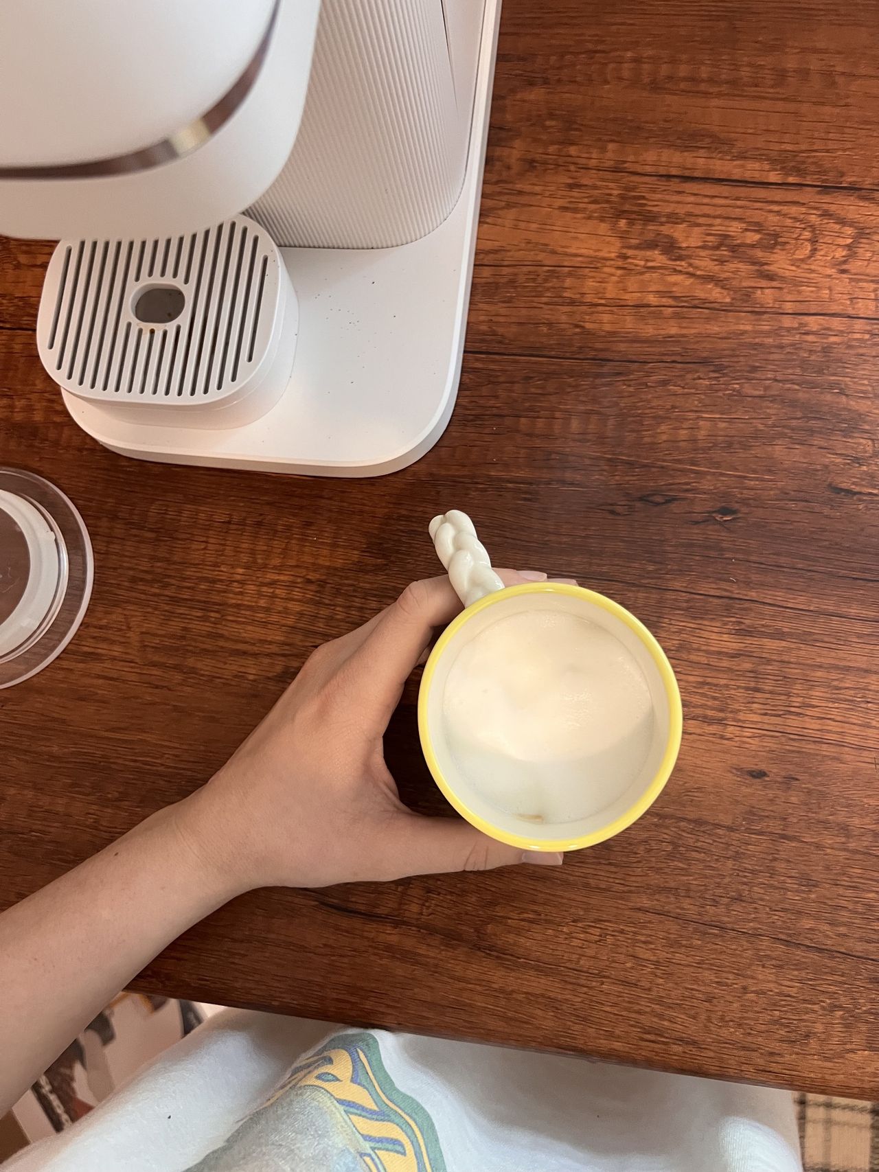 A hand holding a coffee mug with foamy milk in it on a wooden countertop.