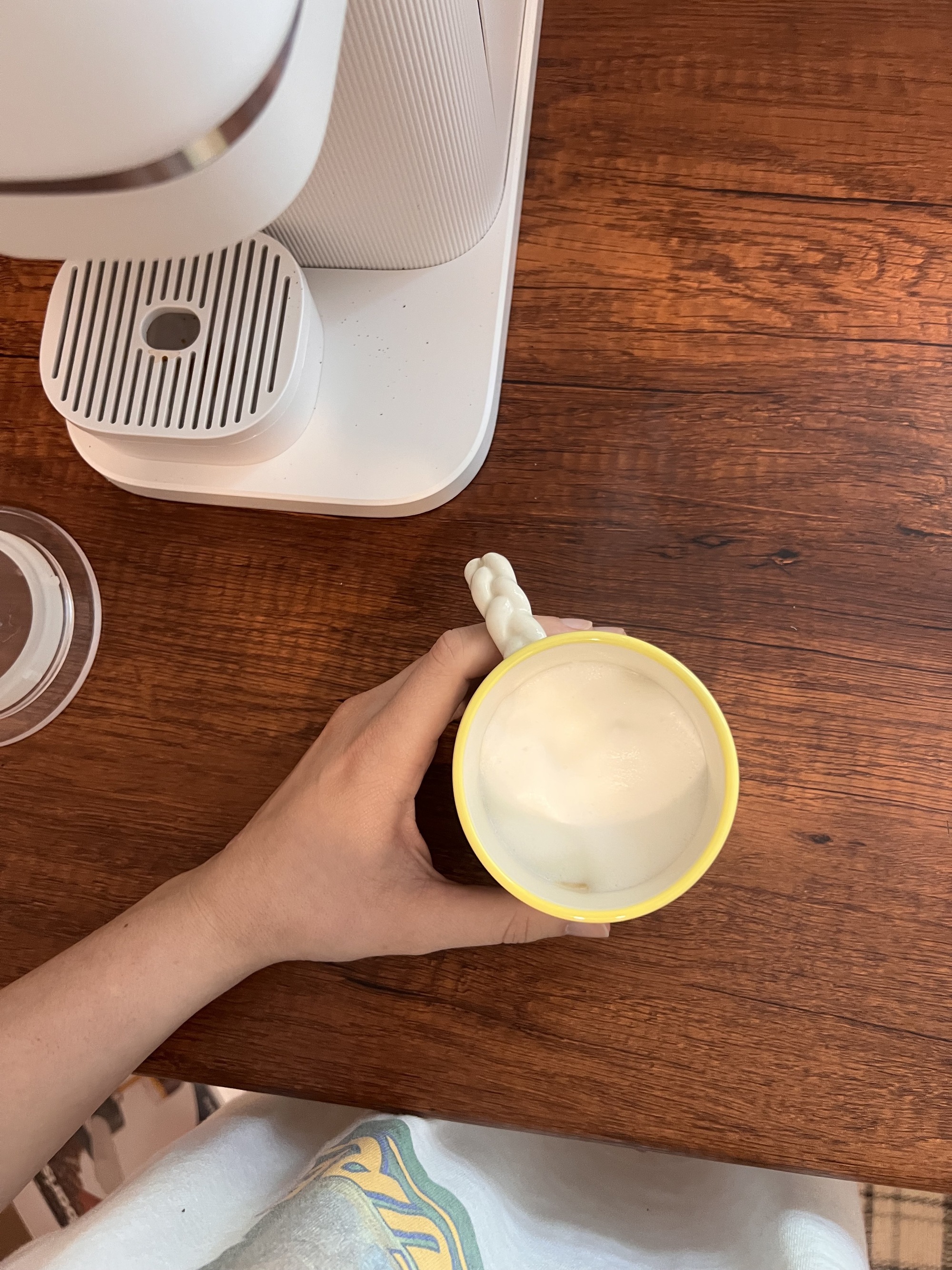 A hand holding a coffee mug with foamy milk in it on a wooden countertop. 