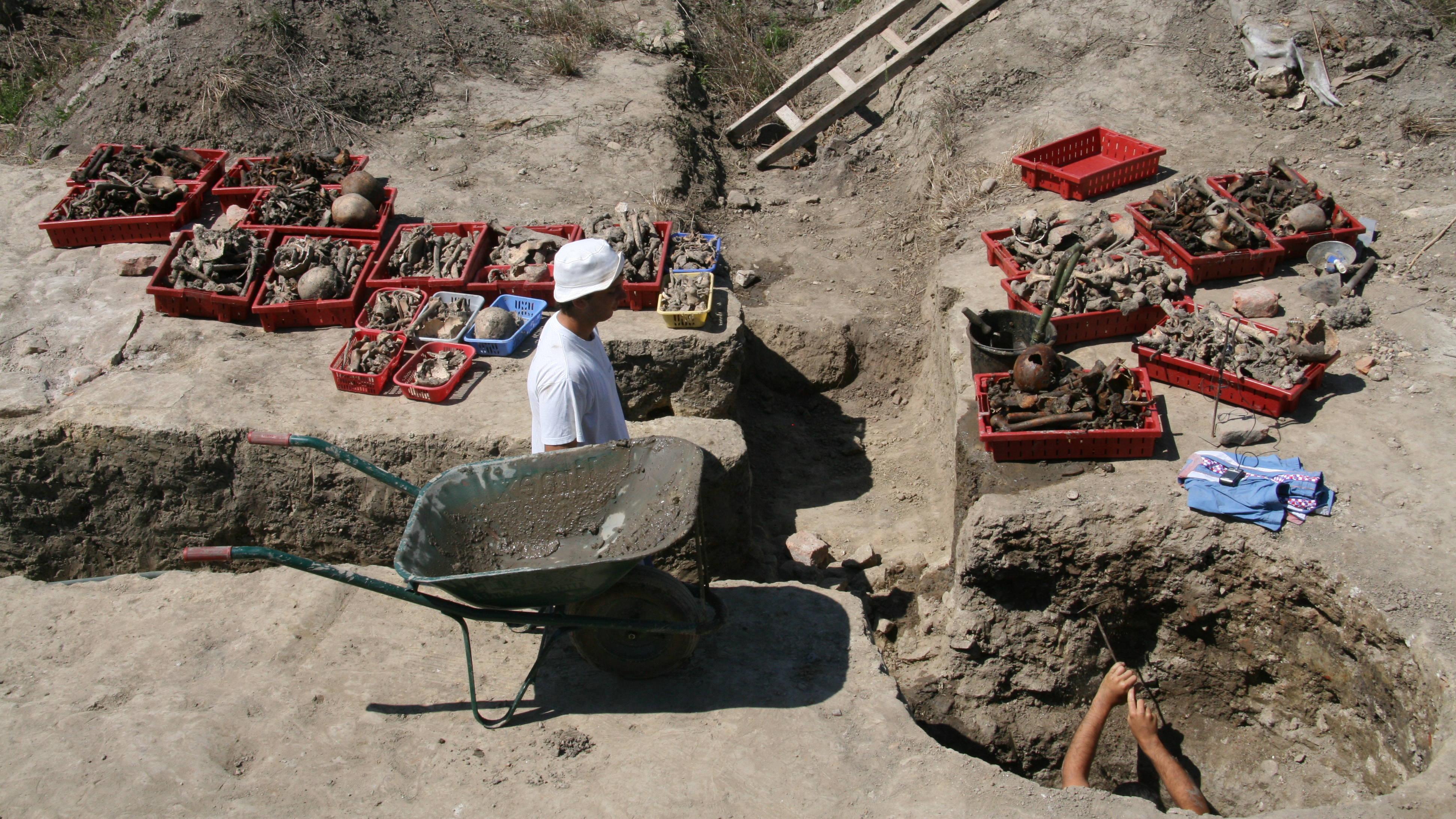 two archaeologists work in a deep trench and well to recover ancient human bones