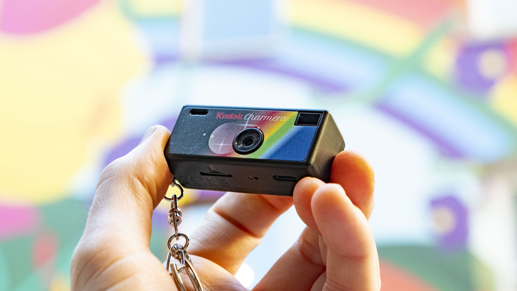 Kodak Charmera compact camera in user's hand with a vibrant graffitied wall backdrop