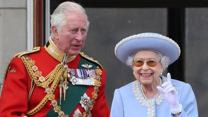 King Charles wears a red military uniform adorned with medal while his late mother Queen Elizabeth wears a baby blue suit jacket with white embroidery