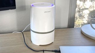 An air purifier on a standing desk next to a laptop